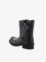 Bota corta de cuero negro, estilo biker, con caña media arrugada y hebillas decorativas metálicas. Presenta un taco bajo y grueso.