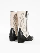Bota corta de cuero sintético color negro y blanco, con punta fina y bordados decorativos.