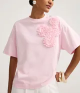Blusa boxy de manga corta, confeccionada en algodón, con cuello redondo y detalles de flores de tejido aplicadas en el hombro y sisa.