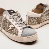 Zapatillas bajas con base blanca, cuerpo con glitter plateado y detalles en gamuza celeste y cuero blanco. Presenta un rayo dorado en el lateral externo.