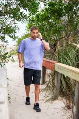 Remeron de corte oversize color violeta lavado, con estampa gráfica en la espalda que representa un paisaje natural con palmeras y un río, junto con el texto 'Part of Nature like you' y 'Glassy Waves x Origen'.