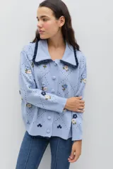 Saco de punto color celeste con bordados florales artesanales, cuello con detalle de volados en contraste y cierre frontal con botones forrados.