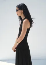 Vestido midi negro sin mangas, con cuello redondo y diseño ajustado en el torso mediante fruncidos laterales, que se abre en una falda evasé fluida.
