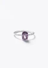 Anillo de plata 925 con una zirconia central de corte ovalado en color violeta y pequeñas piedras blancas engastadas a lo largo del cuerpo del anillo.