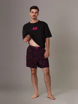 Conjunto de pijama Calvin Klein 1996, compuesto por una remera negra de algodón con cuello redondo, manga corta y logo estampado en el pecho, y un short negro de algodón tejido con bolsillos laterales, cintura elástica con logo y estampado del logo de la marca en color fucsia.
