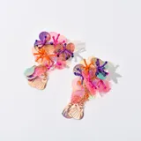 Aros colgantes con base de lentejuelas iridiscentes en tonos rosa, naranja y amarillo. Presentan flores de cuentas violetas y naranjas, y dijes colgantes dorados con forma de concha.