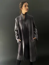 Tapado largo gris de lana merino con bolsillos laterales y corte particular en los hombros.