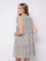 Vestido corto con estampado floral multicolor, cuello tipo camisa y cierre frontal con botones. Presenta volados en las sisas y un diseño de falda con volados en el ruedo.