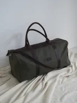 Bolso de lona color verde militar con detalles en cuero marrón. Tiene doble asa de mano y correa de hombro ajustable y extraíble.
