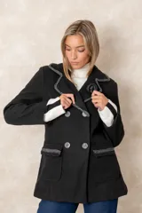 Blazer cruzado color beige, con cierre de cuatro botones frontales. Presenta detalles artesanales de encaje con perlas y cristales en la solapa y en los bolsillos delanteros.