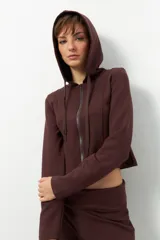 Camperita deportiva color marrón oscuro, ajustada al cuerpo, con capucha y cierre frontal a tono. Presenta costuras verticales que estilizan la figura.