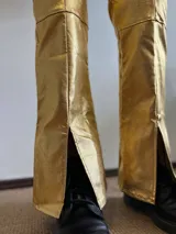 Pantalón dorado de tiro alto, corte ajustado hasta la rodilla y acampanado con aberturas en el ruedo.