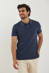 Chomba azul marino de piqué con cuello clásico y mangas cortas. Presenta ribete blanco en cuello y mangas, y cierre de dos botones.