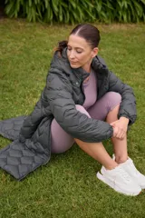 Campera larga color marrón con diseño acolchado, capucha desmontable, cierre frontal con botones a presión, bolsillos laterales con cierre, puños elásticos y cintura ajustable.