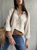 Camisa de color beige con cuello clásico, cierre frontal de botones y mangas largas con puños doblados. Presenta un delicado bordado floral en las mangas.