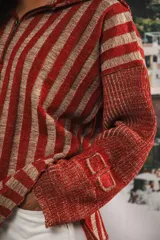 Buzo color beige con rayas horizontales en lurex dorado, cuello con medio cierre, corte oversized y logo tejido en el puño.