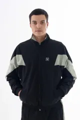 Campera negra de nylon con recortes en forma de V en color gris en las mangas. Tiene cuello mao, cierre frontal, puños y cintura elásticos, bolsillos laterales y logo estampado en el pecho y en la manga izquierda.