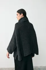 Sweater tipo poncho de tejido grueso en color gris oscuro, con cuello alto tipo polera y mangas anchas. Presenta un diseño holgado y texturizado.