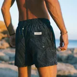 Short de baño negro con estampado botánico de hojas en líneas finas blancas. Cuenta con cintura elástica con cordón ajustable, dos bolsillos laterales y uno trasero.