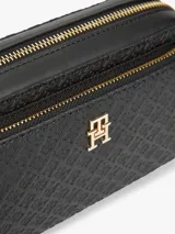 Cartera tipo cámara de poliuretano color negro, con diseño texturizado en bajo relieve con monograma TH, herrajes dorados, cierre de cremallera y correa cruzada extraíble.