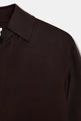 Camisa de manga larga color marrón oscuro, con cuello solapa, escote pico pronunciado y bajo asimétrico redondeado.