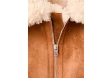 Chaqueta estilo aviador de ante sintético en color marrón con detalles de borrego sintético en el cuello, los puños, la solapa y el dobladillo inferior, con bolsillos laterales y cierre frontal con cremallera.
