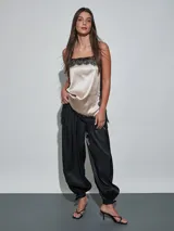 Pantalón negro de satén, de corte fluido y estilo bombacho, con cintura elástica y puños fruncidos en los tobillos con detalle de lazo.