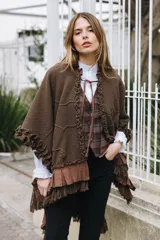 Ruana de punto color bordó con textura marcada, cuello con volados y lazo frontal regulable. Presenta terminaciones con volados de lino y flecos en el ruedo, con un diseño artesanal de silueta amplia y fluida.