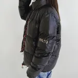 Campera puffer reversible de color negro con acabado brillante. Presenta cuello alto, cierre frontal y un diseño interior con estampado animal print. Incluye logo de la marca en la manga.