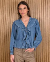 Camisa de denim de algodón ligero, con cuello en V adornado con grandes volados frontales y cierre de botones. Presenta mangas largas con puños elásticos fruncidos.