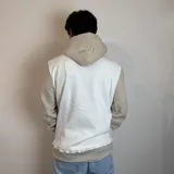 Canguro con capucha de diseño bicolor, combinando paneles en color blanco y beige. Presenta un bolsillo frontal tipo canguro y el logo de la marca bordado en el pecho.