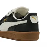 Championes Puma modelo Palermo, con diseño de perfil bajo en color negro con detalles en blanco y suela de goma color caramelo. Presentan el logo de la marca en dorado en el lateral y una lengüeta distintiva.
