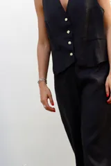 Chaleco de lino en color beige, con escote en V, cierre frontal con botones y bolsillos delanteros decorativos.