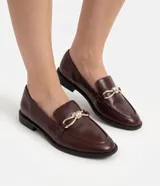 Zapato mocasín Satinato confeccionado en poliuretano color bordó, con tacón bajo, punta redonda y detalle metálico dorado en el empeine.