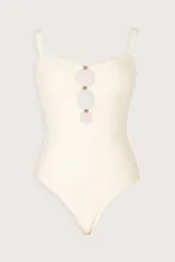 Malla enteriza de color crema con diseño strapless, fruncidos en el frente y tres aberturas circulares verticales separadas por herrajes metálicos brillantes. Presenta tirantes finos removibles.