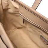 Cartera tipo tote bag de mujer, color taupe, con textura de cuero granulado. Presenta dos asas de mano y una correa larga desmontable y regulable. Tiene un parche frontal con el logo "XL" y herrajes metálicos color níquel.