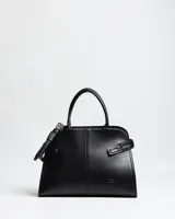 Cartera de mano de símil cuero color negro, con diseño estructurado, doble asa rígida y correa ajustable desmontable. Cuenta con costuras verticales decorativas en el frente, tiras laterales con broches y el logo metálico de la marca en la esquina inferior.