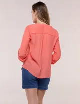 Blusa de calce relajado color salmón, confeccionada en tela liviana con textura sutil. Presenta escote en V con abotonadura frontal, bolsillo parche en el pecho, mangas largas regulables con presilla y ruedo con opción de anudar en el frente.