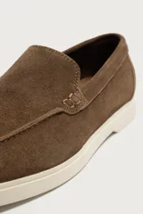Mocasines casuales para hombre, fabricados en piel con acabado en serraje color marrón, de corte liso con detalle de bordón y suela blanca a contraste.