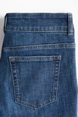 Jeans de denim azul de tiro bajo con leve elasticidad. Presentan un corte ajustado hasta el muslo y acampanado desde la rodilla. El cierre es frontal con botones en una pretina prolongada y cuenta con bolsillos delanteros de parche y bolsillos traseros.