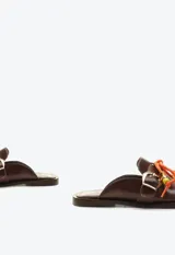 Zueco mocasín de cuero marrón, con taco plano, hebilla metálica dorada lateral y detalle de cordón naranja con cuentas decorativas en el empeine.