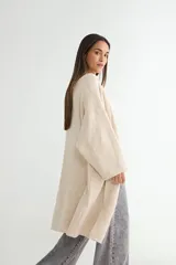 Saco tipo cárdigan largo de tejido de punto, color beige, con diseño abierto sin botones, mangas largas amplias y corte recto.