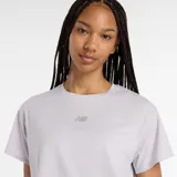 Remera deportiva New Balance color lila claro, de corte crop y holgado, con logo pequeño en el pecho.