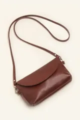 Cartera tipo sobre de cuero color marrón, con solapa frontal redondeada que presenta un detalle circular grabado. Incluye correa larga ajustable y extraíble, cierre principal y broche de seguridad.