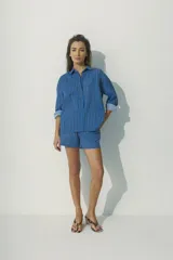 Camisa de corte relajado con diseño de rayas verticales en tonos rojos, marrones y blancos. Presenta cuello clásico, cierre frontal con botones al tono y mangas largas con puños que permiten un estilo arremangado.