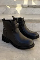 Bota corta de cuero negro con diseño de caña media, cierre lateral y detalle de tira horizontal sobre el empeine. Posee suela de goma gruesa y puntera redondeada.