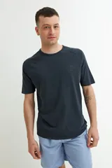 Remera de manga corta color azul oscuro o negro deslavado, con cuello redondo y corte raglán. Presenta un pequeño estampado en relieve o tono sobre tono en el pecho con texto y un símbolo.