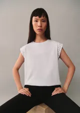 Camiseta blanca de algodón con cuello redondo y mangas cortas con tachas decorativas en los hombros.