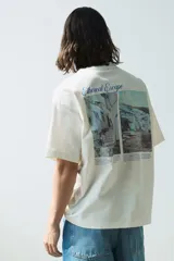 Remera color hueso de corte oversized, confeccionada en tejido de algodón pesado. Presenta cuello redondo acanalado, hombros caídos y estampado pequeño con la frase "Ethereal Escape" en el lado izquierdo del pecho.