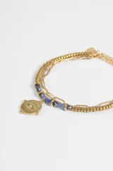Pulsera de acero quirúrgico plateado de doble tira, una de cadena eslabonada y otra con cuentas de metal y piedras azules. Cuenta con un dije colgante circular con diseño de ojo y detalles grabados.